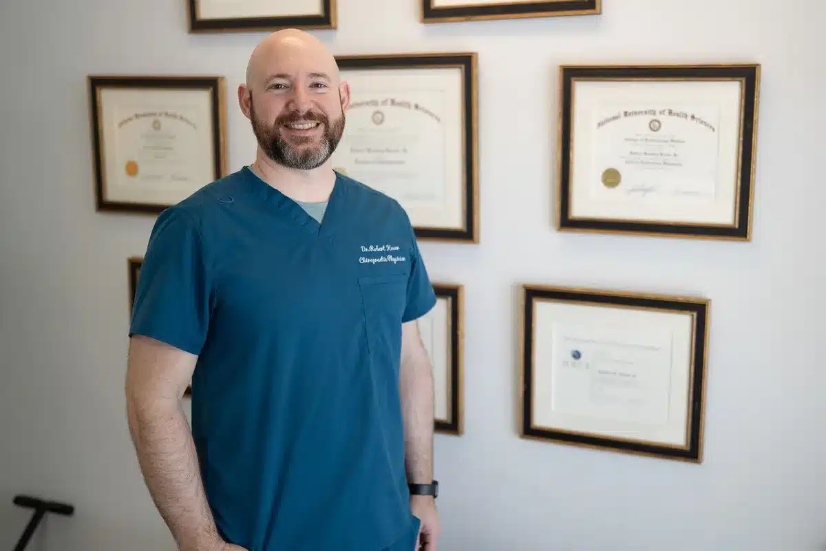 Dr. Bobby Koser, DC, chiropractic physician, standing beside the framed certification wall at HealthSpine Chiropractic in Carrollwood, Tampa.