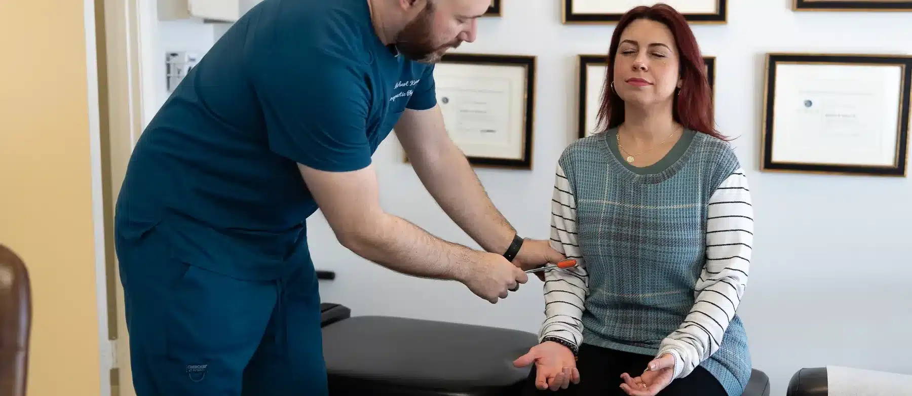 Dr. Bobby Koser, DC, chiropractic physician, testing a seated patient&rsquo;s reflexes during a neurological examination at HealthSpine Chiropractic in Carrollwood, Tampa.