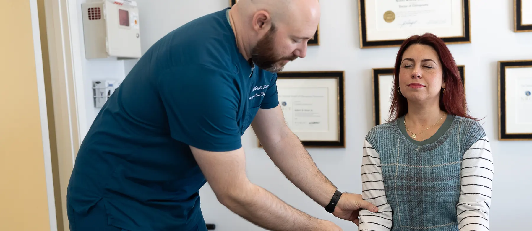 Dr. Bobby Koser, DC, chiropractic physician, examining a seated patient&rsquo;s arm and shoulder at HealthSpine Chiropractic in Carrollwood, Tampa.