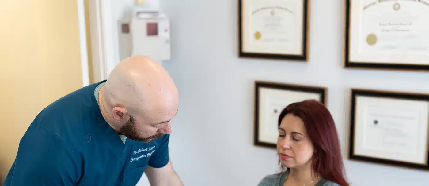 Dr. Bobby Koser, DC, chiropractic physician, examining a seated patient’s shoulder and arm at HealthSpine Chiropractic in Carrollwood, Tampa.