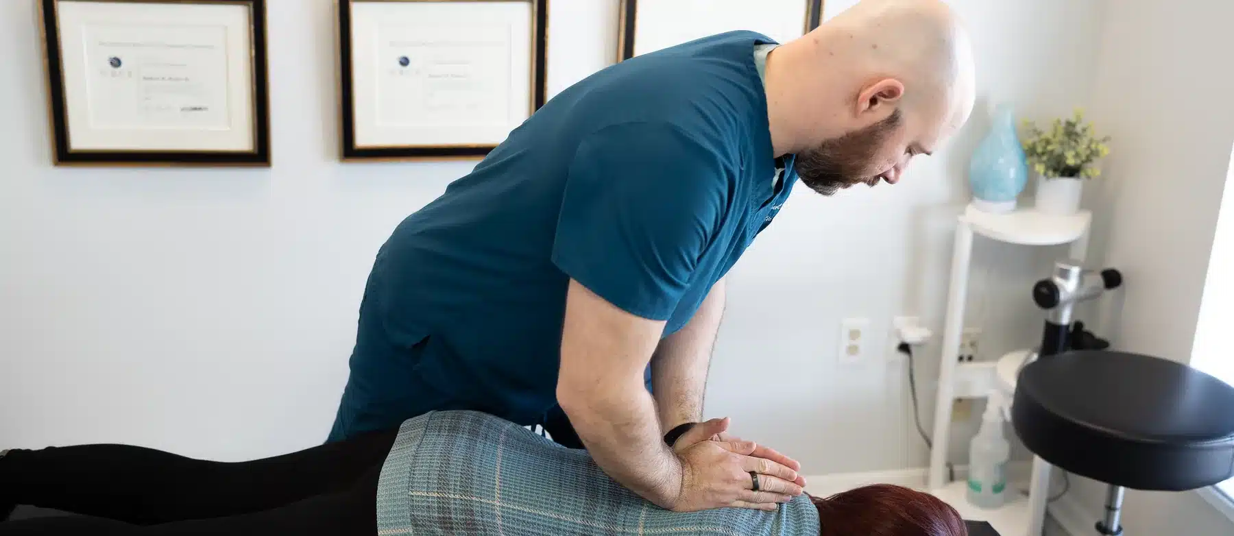 Dr. Bobby Koser, DC, chiropractic physician, treating a patient&rsquo;s upper back on the adjusting table at HealthSpine Chiropractic in Carrollwood, Tampa, with his framed certifications on the wall behind him.